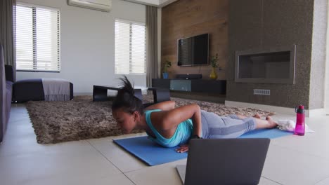 mujer de raza mixta haciendo ejercicio en una alfombra con computadora portátil