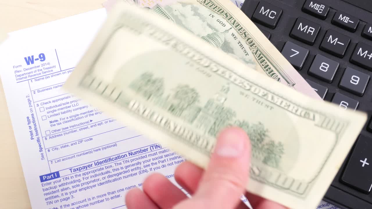 las manos de los hombres lanzan varios billetes de cientos de dólares sobre la mesa con una calculadora y un formulario de impuestos.