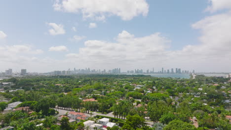 Forwards-fly-above-residential-neighbourhood-with-family-houses-and-residences-surrounded-by-greenery.-Skyline-with-skyscrapers-in-distance.-Miami,-USA