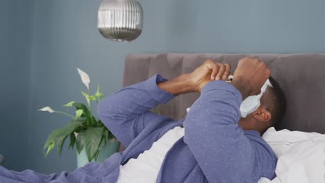 Video-of-african-american-man-lying-on-bed-with-cleansing-face-mask-putting-cucumber-slices-on-eyes