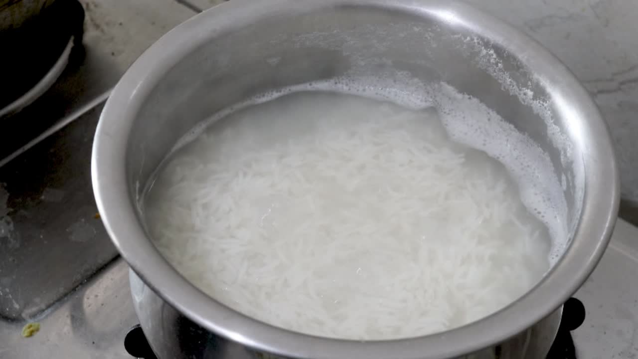 Video ravvicinato di riso bianco che bolle in acqua in una pentola d'acciaio con vapore