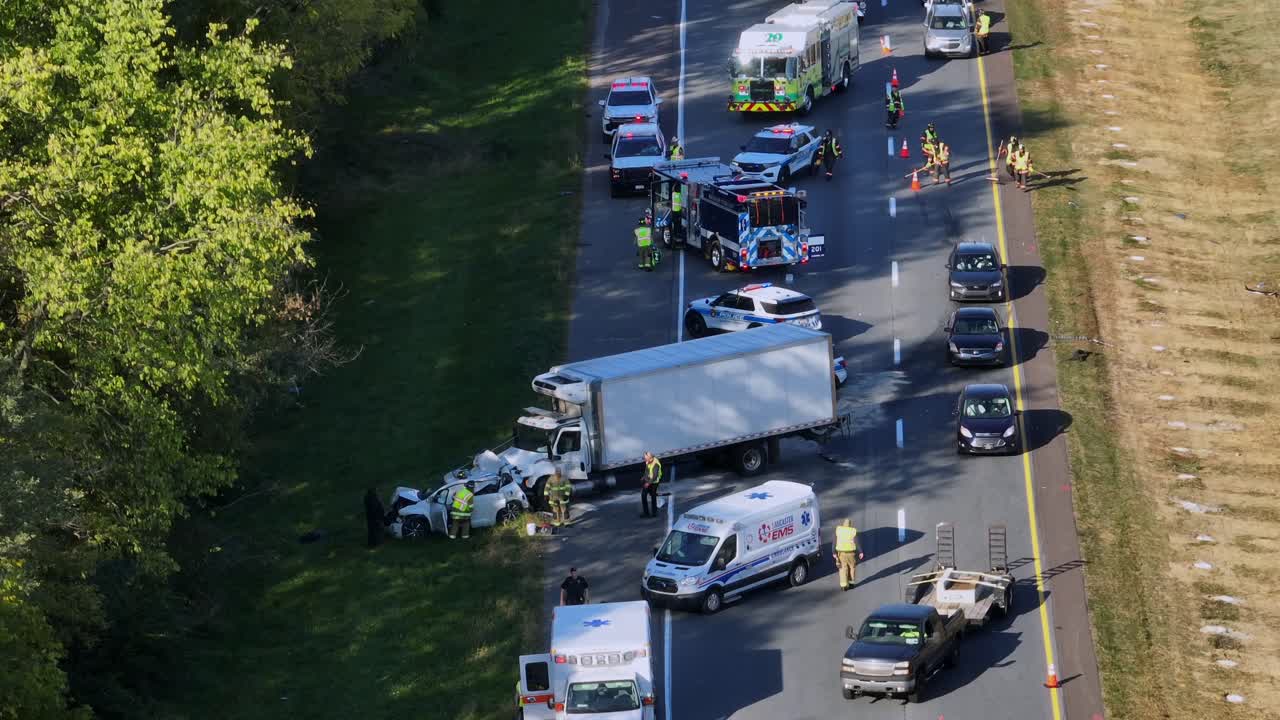 Cars overtaking on street after vehicle accident in america. Firemen cleaning highway after crash. Aerial static shot. Injured people on sunny autumnal day in american suburb town.