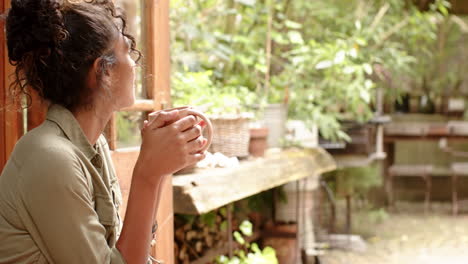 woman enjoying coffee at home, gazing thoughtfully out window at garden, copy space