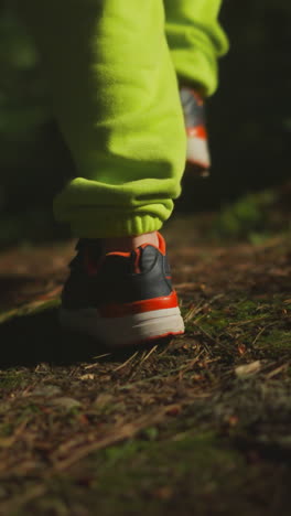 niño pequeño en pantalones de deporte verdes claros y zapatos deportivos camina solo en el bosque de la noche. niño vaga a lo largo del camino del bosque iluminado en busca de un campamento familiar