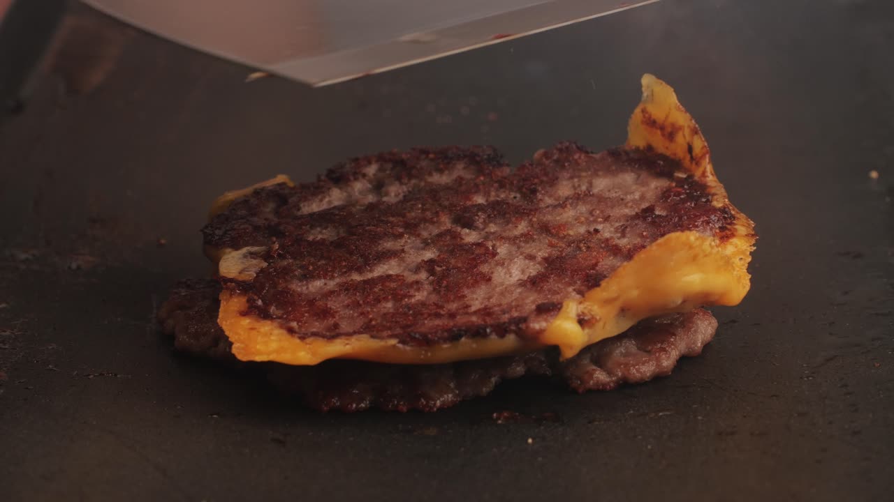Cooking American fat smash burger with cheese slice on top on grill close-up. Beef or pork cutlet smashing by burger press. The chef in kitchen of the restaurant making cutlets for burgers - smash burger beefsteak. Fast and street food concept.