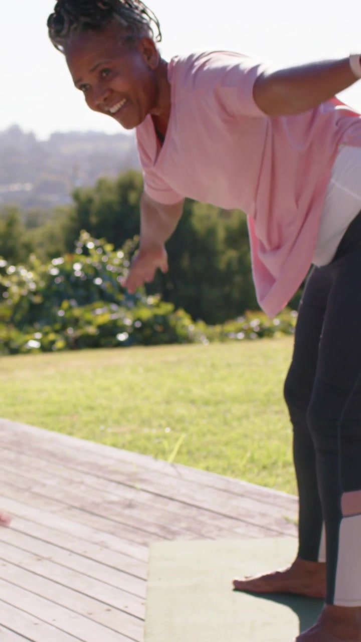 Video verticale: Due donne in rosa si allungano al sole, piegandosi lateralmente sul ponte, preparandosi con tappetini da yoga.