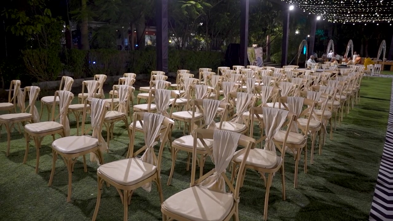 Uno spazio per eventi all'aperto allestito con file di sedie eleganti disposte su un prato curato sotto luci decorative a filo. Tavoli e un'area evento decorata sono visibili sullo sfondo