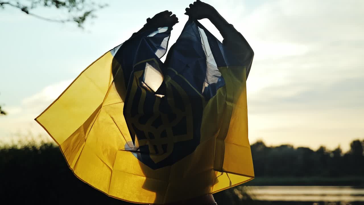 Woman waves Ukrainian flag behind her as it glows in golden sunset light
