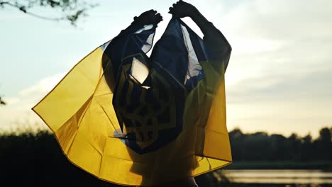 woman waves ukrainian flag behind her as it glows in golden sunset light