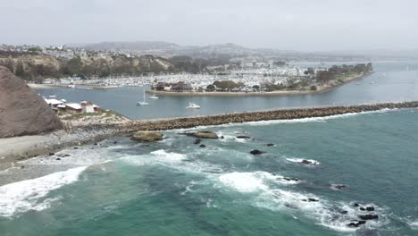 pushing in dolly aerial of dana point california with its yachts boats paddle boarders clean beaches elegant homes sea walls and turquoise water from the air and bird's eye perspective