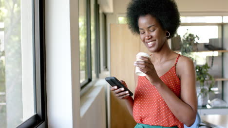 Mujer-De-Negocios-Afroamericana-Informal-Tomando-Café-Y-Usando-Un-Teléfono-Inteligente-En-La-Oficina,-Cámara-Lenta