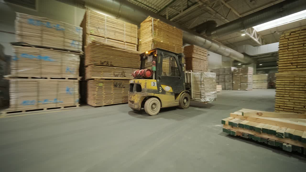 Carretilla elevadora moviendo palés de madera en un gran almacén industrial.