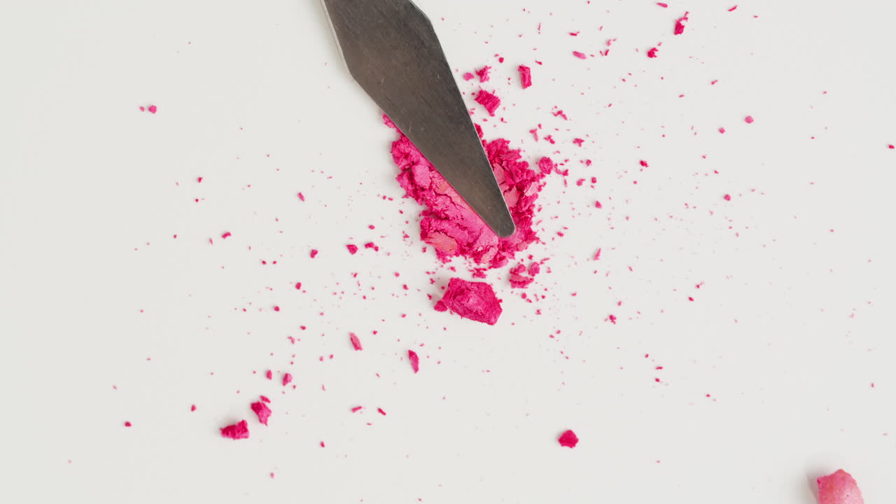 Pink eyeshadow powder spilled from a spatula