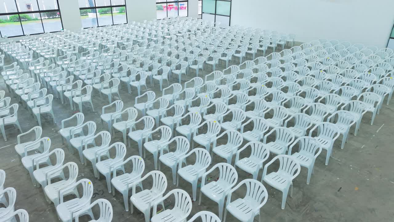 Wide cinematic view of an empty modern event hall filled with neatly arranged white plastic chairs, symbolizing scale, organization, and anticipation before a large conference or public gathering