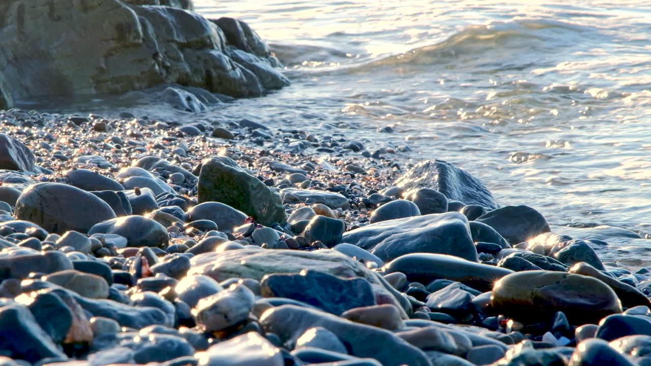 Smooth glistening coastal rocks at sunrise as relaxing waves lap onto shoreline