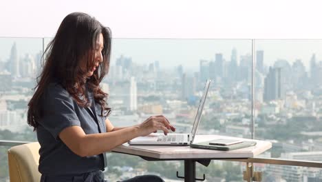 thoughtful asian woman pondering on creative ideas for writing essay, reading emails during working hard on laptop with wireless internet in office lounge on skyscraper and blur background city.