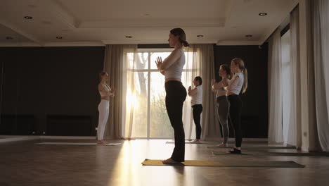 in slow motion a yoga instructor conducts a group lesson for women of different ages and weight categories thin and full in the gym in the morning in the sun. the glare of the sun on the floor