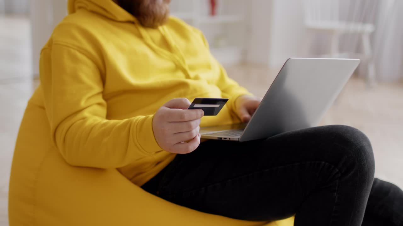 Uomo irriconoscibile che fa acquisti online usando un laptop e una carta di credito al chiuso