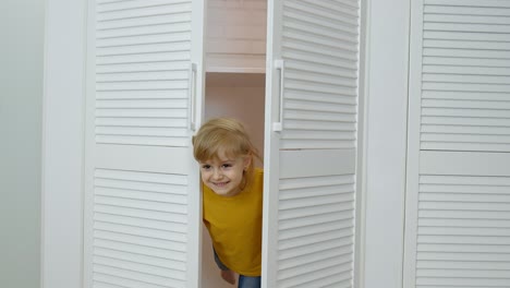 Little-blonde-child-girl-wearing-jeans,-orange-jacket-opening-wardrobe-and-looking-at-camera-at-home