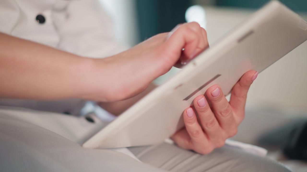 Caucasian nurse hands holding tablet reviewing patient record via touchscreen at home bedside, white uniform, soft natural light, focused fingers navigating telemedicine app, documentation visible
