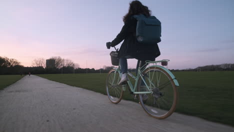 Rear-profile-follow-shot-of-young-woman-cycling-on-a-gravel-path-at-sunset