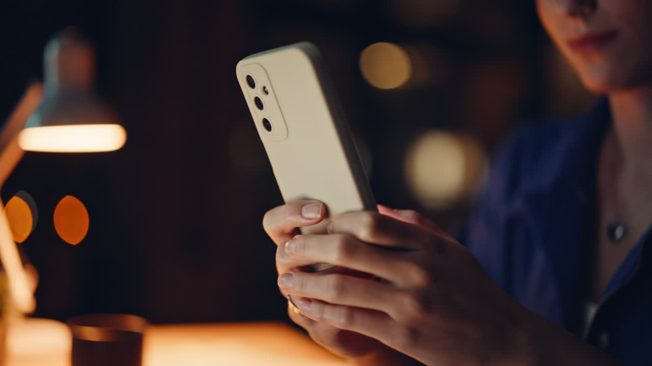 Cheerful brunette messaging smartphone at night home closeup. Happy woman sms