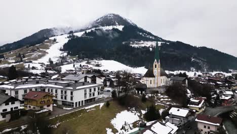 snowy mountain peak and township with church tower of kirchberg, aerial drone view