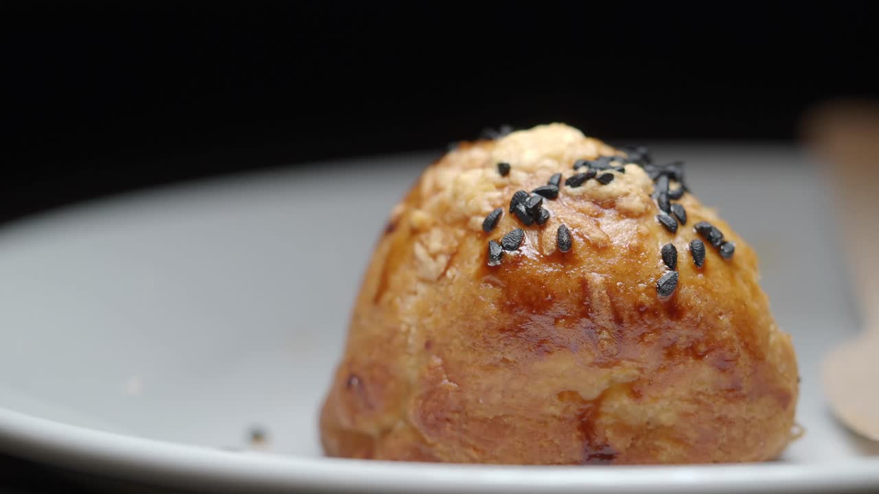 Hand Picking Up a Golden Baked Pastry with Black Sesame Seeds