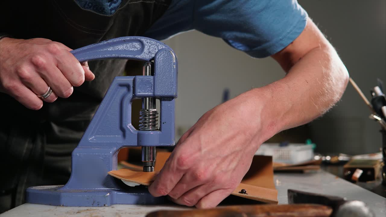 Leatherworker using a hand-operated hole punching machine.