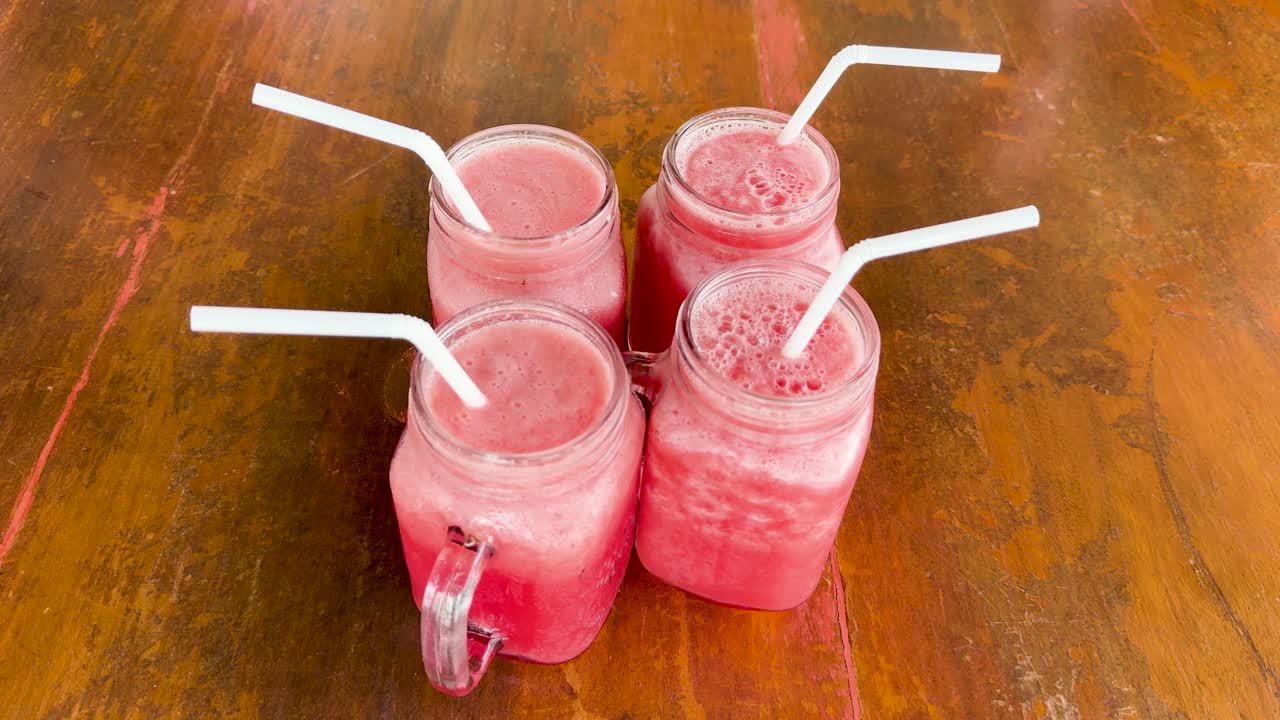 Three pink cocktails with straws in mason jars on a wooden table, captured at a clifftop restaurant in Phuket, Thailand