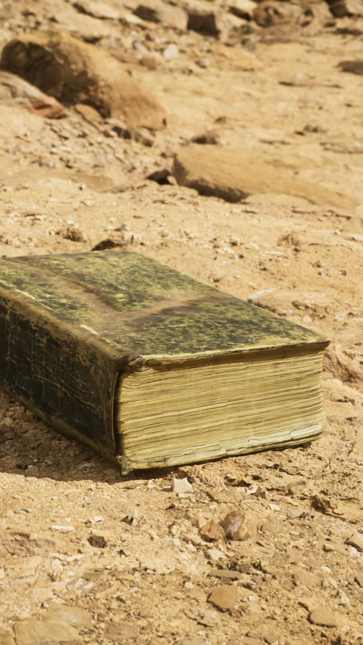 Old book resting on dusty ground in a deserted area under bright sunlight