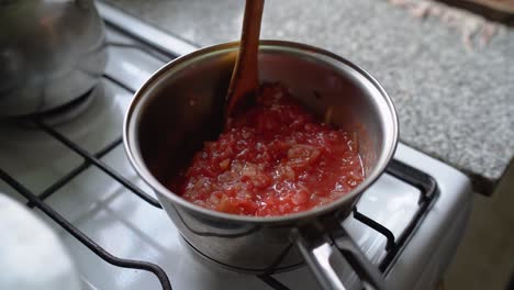 cooking and stirring tomato sauce with a wooden ladle