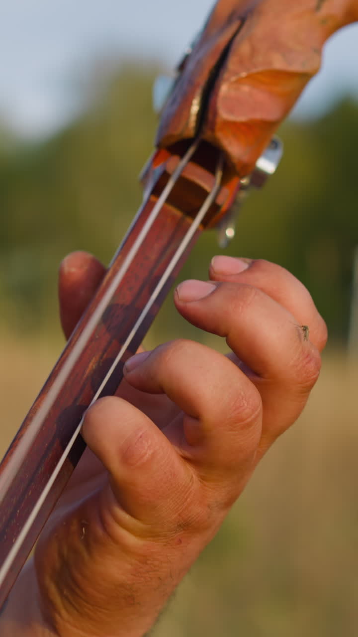 Folk musician presses strings on deck playing ikili on field closeup slow motion. Man performs at Altai ethnic music concert. National instruments