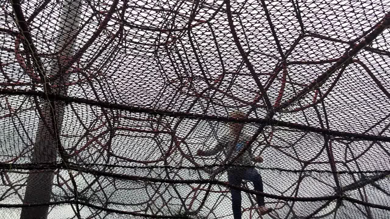 Young caucasian girl having fun by herself inside huge climbing tower at playground - Handheld from down below