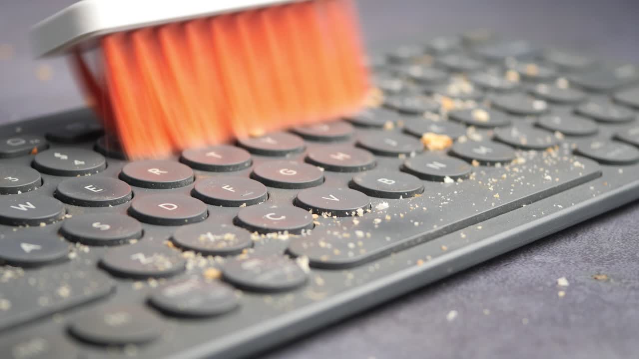 Cleaning crumbs off a dirty keyboard with a brush