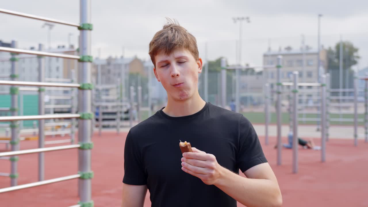 Young man taking a snack candybar after sport fitness on outdoor exercise ground, active lifestyle and self improvement