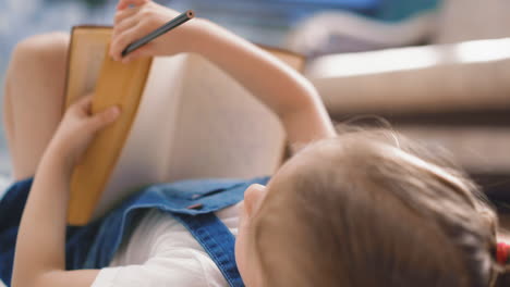 niña con libro y lápiz hace la tarea en el suelo
