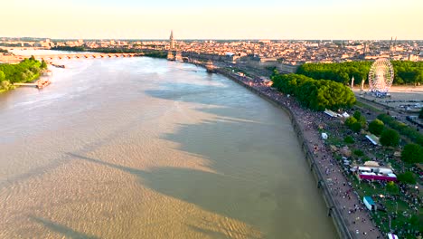 garonne river and wine fair with ferris wheel full of crowds in bordeaux france, aerial pan right and left shot