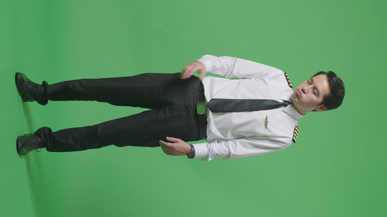 녹색 스크린 배경 스튜디오에 서 있는 동안 두통을 가진 아시아 남자 조종사의 몸이 가득 차 있습니다.