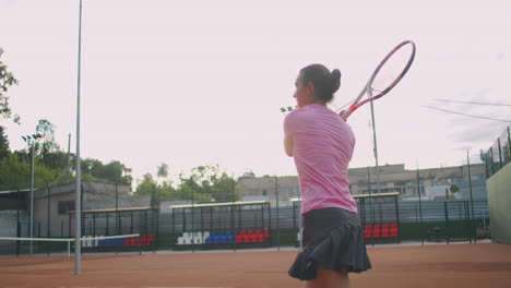 slow motion commercial footage of tennis practice through the tennis court net. straight view of a female athlete playing the tennis game. a teenage sportsman is hitting the ball during sport training