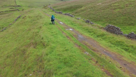 back view of a backpacker trekking up peak district national park in england on a rainy day