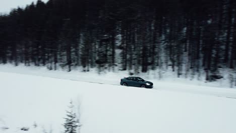 Un-Coche-Eléctrico-Circula-Por-Una-Carretera-Cubierta-De-Nieve-En-El-Círculo-Polar-ártico-Durante-Una-Nevada,-Disparo-De-Un-Dron