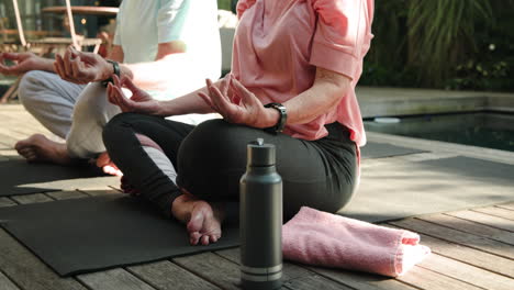 Senior couple meditating outdoors on yoga mats by pool, enjoying relaxation