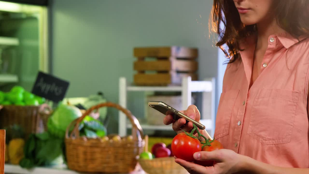 mujer con un tomate y usando un teléfono móvil