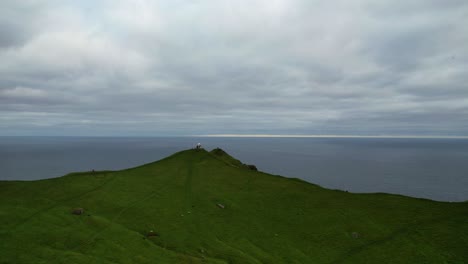 aerial tracking forward over kallur lighthouse reveals hiking couple overlooking the ocean, faroe islands