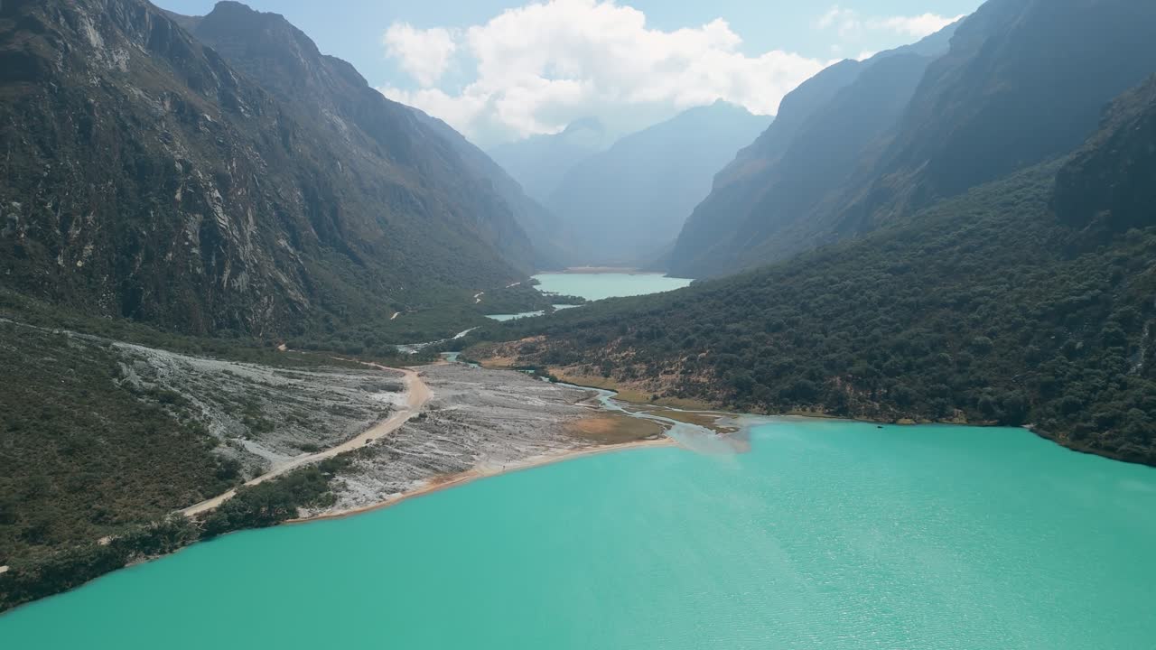 Aerial flyover revealing two turquoise glacial lakes, Chinancocha and Orconcocha, nestled in the Andes within Huascarán National Park, Peru