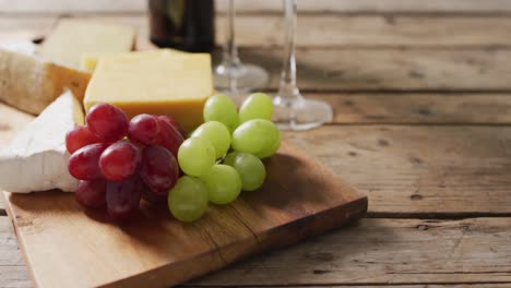 Video-of-cheeses-and-grapes-on-board-wine-bottle-and-glasses-on-wooden-table,-with-copy-space