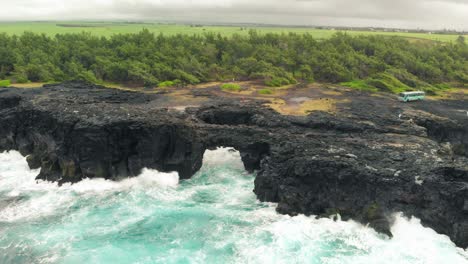 tourists bus parked as waves crash against the rocks of the pont naturel in mauritius