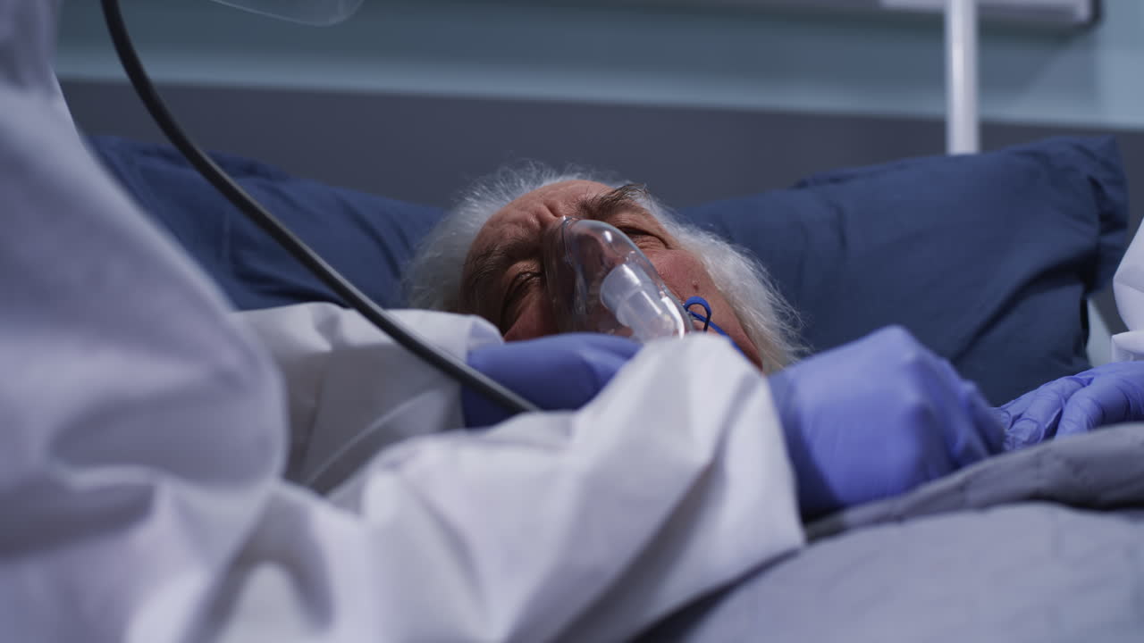 Medical staff attending to an elderly patient in a hospital bed with an oxygen mask