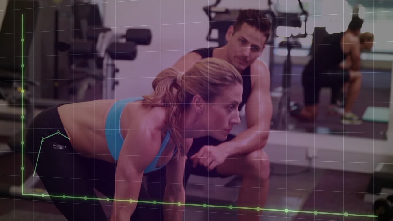 Woman gripping barbell, deadlifting on green gym mat for form, trainer cueing while graphs tracking